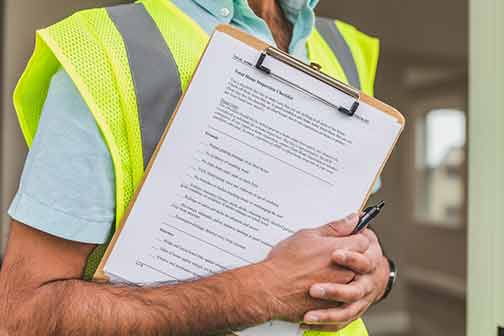 A plumber wearing a yellow safety vest, a black pen, and an inspection checklist.