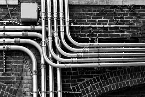 Grey pipelines mounted on a black brick wall.