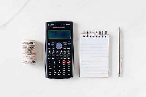 A calculator, pen, notebook, and rolled paper money