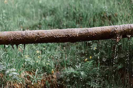 Rusted metal leaking pipe above a grassy meadow.