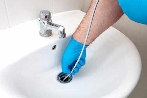 a man using a plumbing snake on his drain