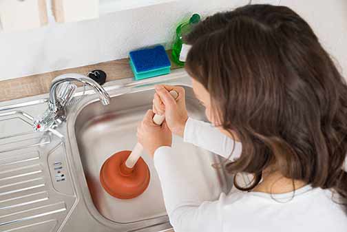 a woman plunging a kitchen drain clog