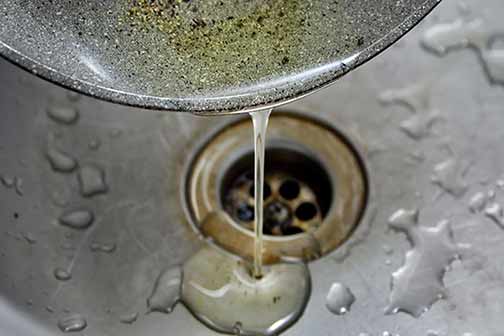 pouring grease down a drain in a restaurant.